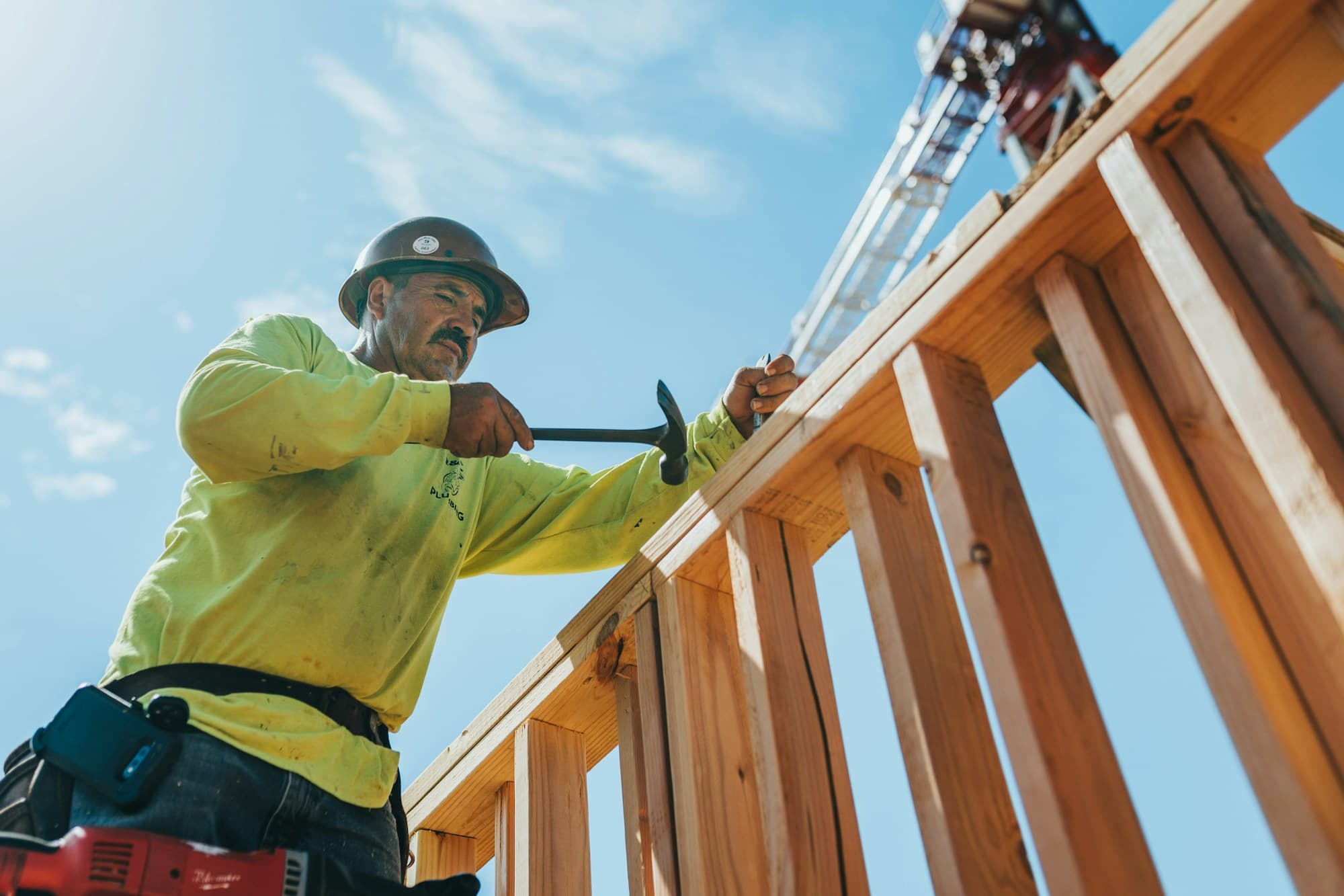 A builder framing a timber structure under a blue sky