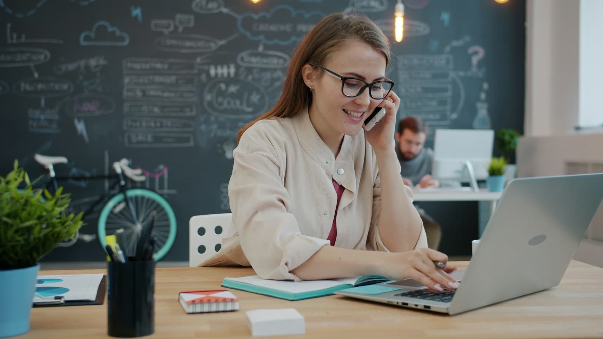 A broker on a phone call at her laptop in a bright office